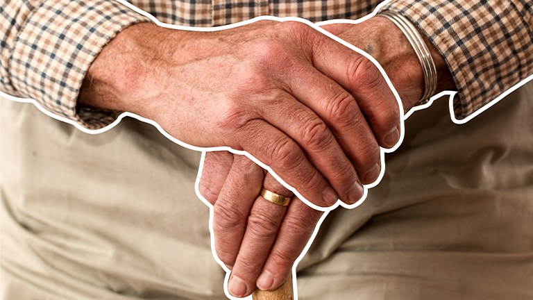 Imagem de uma pessoa mais velha, com calça bege e blusa listrada apoiando uma mão na outra, mãos mais velhas, representando a aposentadoria